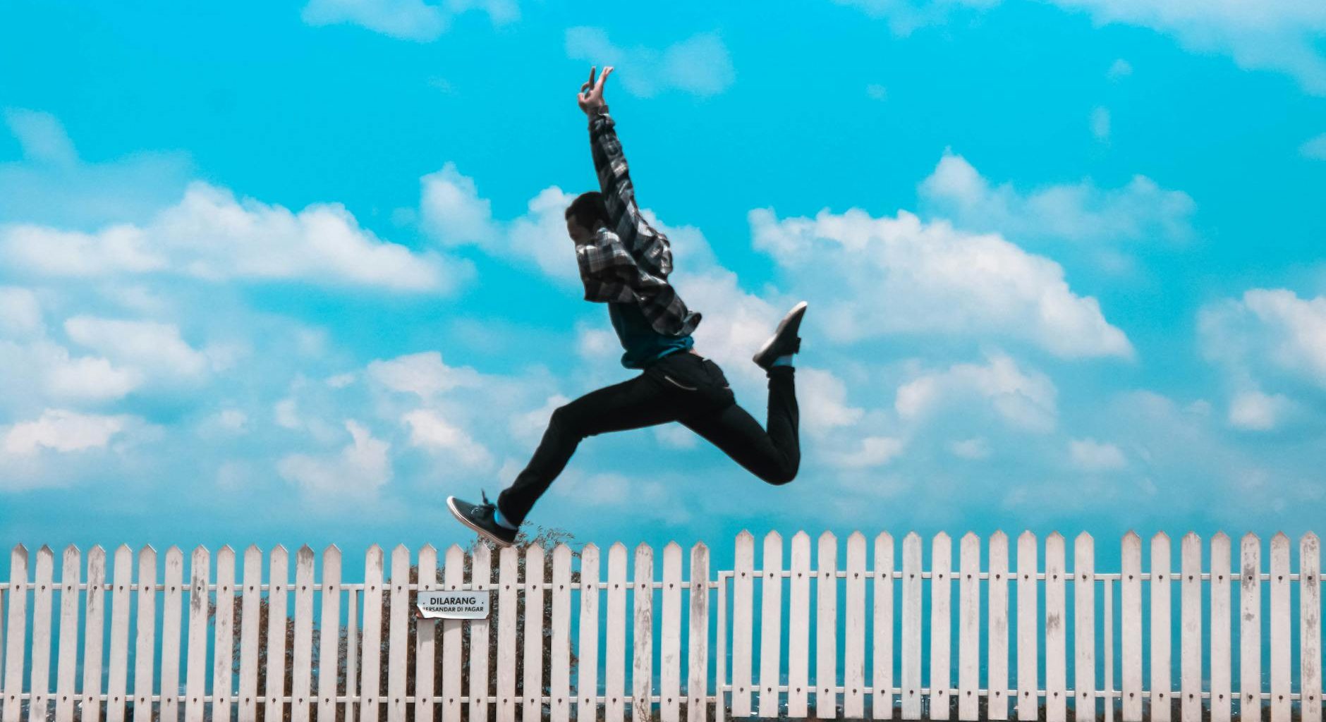 man jumping over white fence
